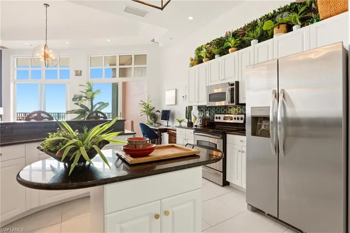 Kitchen featuring stainless steel appliances, white cabinetry, a kitchen island, dark stone counters, and hanging light fixtures