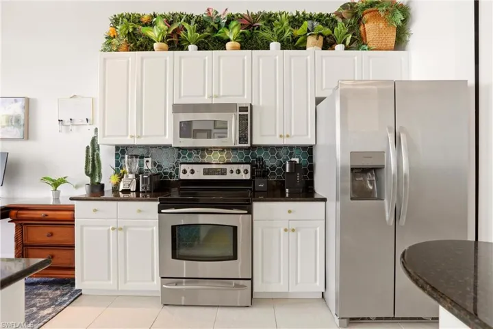 Kitchen with stainless steel appliances, dark stone counters, white cabinetry, and backsplash