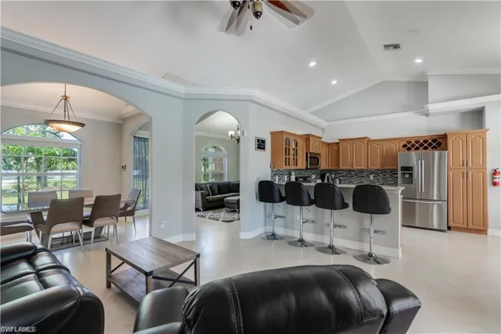 Living area featuring vaulted ceiling, arched walkways, ceiling fan, and ornamental molding