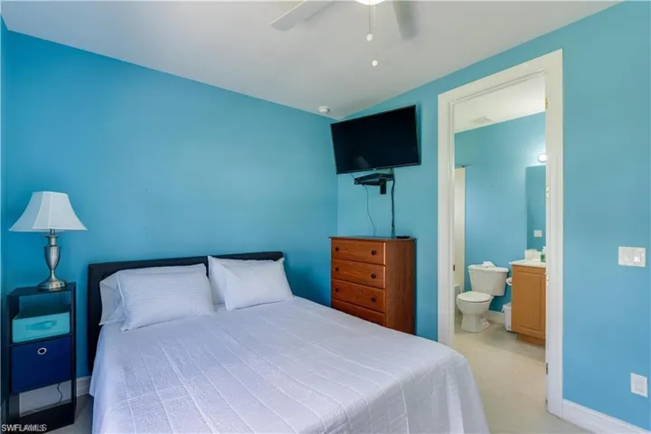 Carpeted bedroom with ceiling fan, lofted ceiling, and ensuite bath