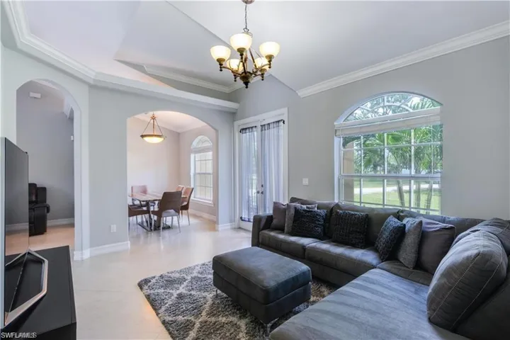 Living area featuring ornamental molding, arched walkways, a chandelier, light tile patterned flooring, and a tray ceiling