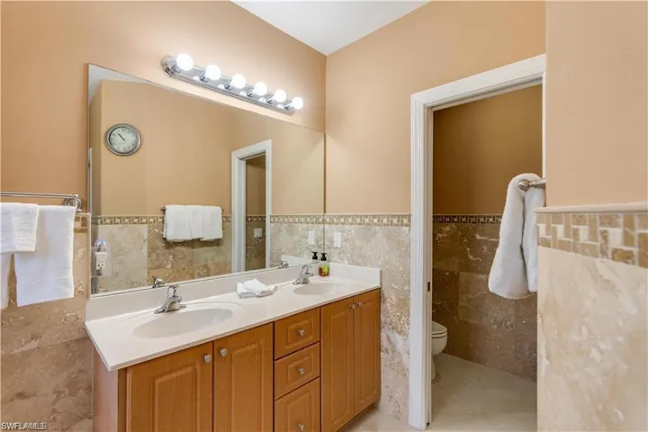 Bathroom featuring tile walls, double vanity, wainscoting, and light tile patterned flooring