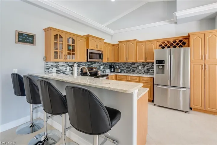 Kitchen with a breakfast bar area, appliances with stainless steel finishes, glass insert cabinets, tasteful backsplash, and vaulted ceiling