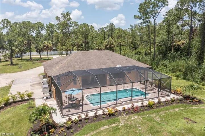 Swimming pool featuring glass enclosure, a sunroom, a lawn, and a patio area