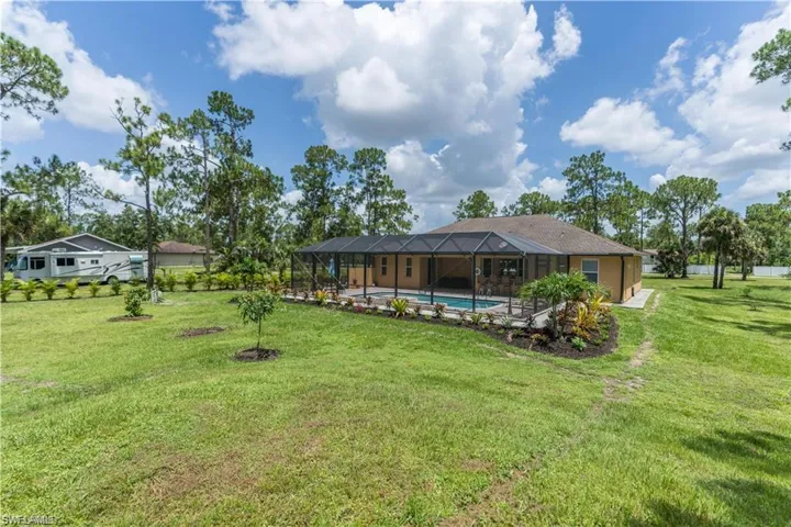 Rear view of house featuring glass enclosure, a sunroom, a yard, and an outdoor pool
