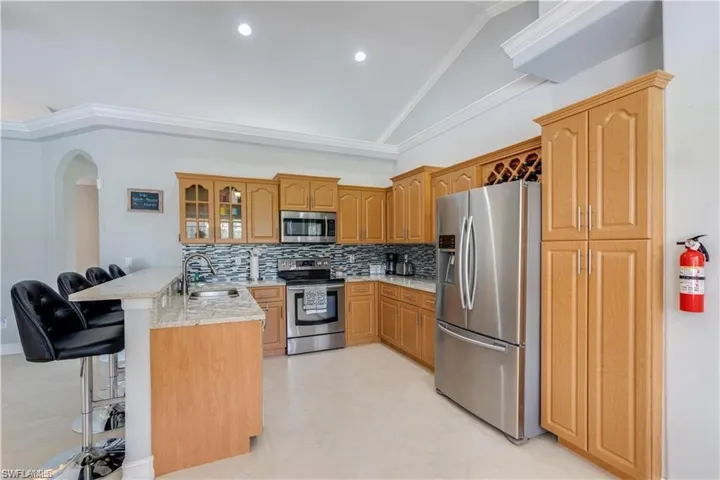 Kitchen featuring a kitchen bar, a peninsula, glass insert cabinets, stainless steel appliances, and backsplash