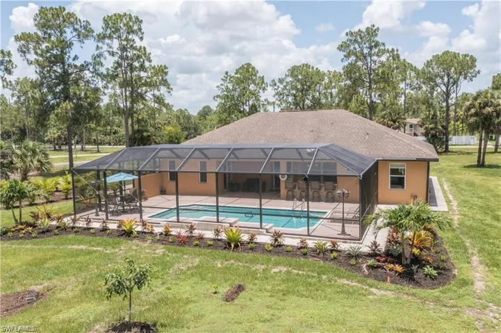 Swimming pool featuring a lanai, a lawn, view of scattered trees, a sunroom, and a patio