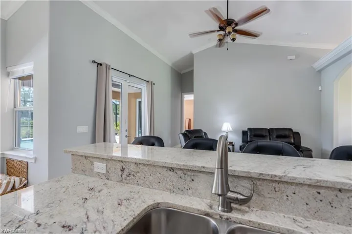Kitchen with crown molding, light stone countertops, french doors, lofted ceiling, and a ceiling fan