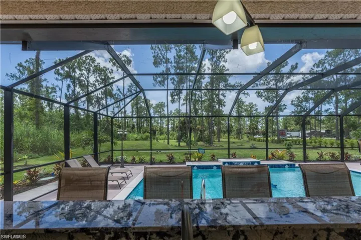 Swimming pool featuring glass enclosure, a sunroom, a patio area, and view of scattered trees