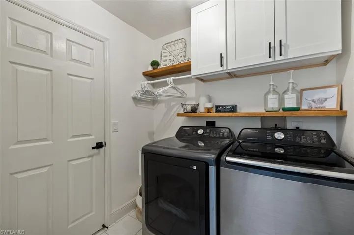 Laundry room with cabinets, a textured ceiling, washer and clothes dryer, and light tile patterned floors