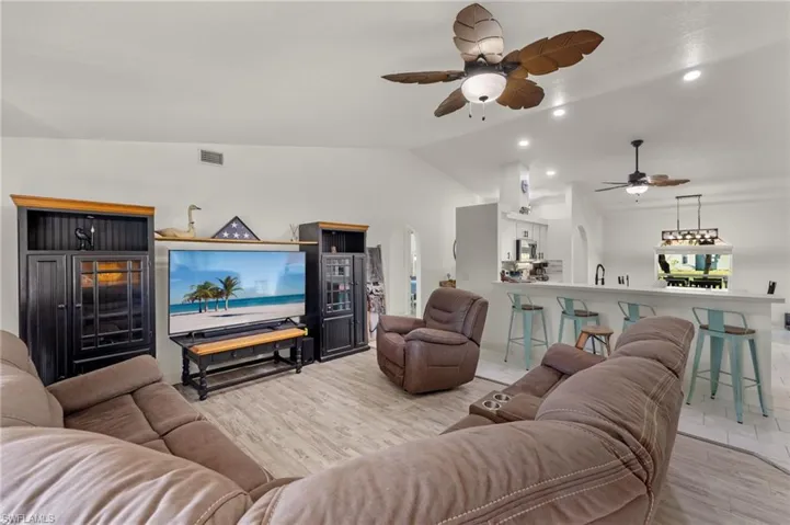 Living room featuring ceiling fan, lofted ceiling, and light wood-type flooring