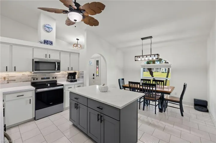 Kitchen with stainless steel appliances, backsplash, pendant lighting, gray cabinets, and white cabinetry