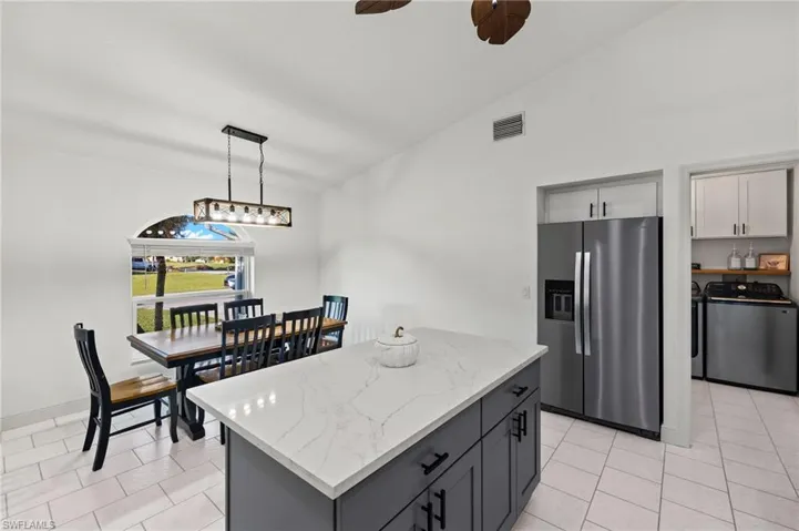 Kitchen featuring stainless steel fridge with ice dispenser, separate washer and dryer, vaulted ceiling, gray cabinets, and decorative light fixtures