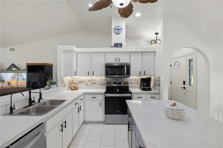Kitchen with lofted ceiling, decorative backsplash, sink, white cabinets, and appliances with stainless steel finishes