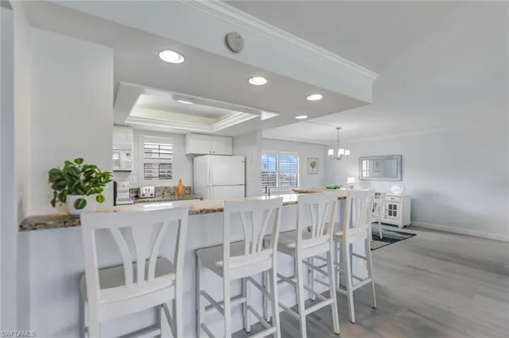 Kitchen featuring recessed lighting, a breakfast bar area, white cabinets, light stone countertops, and white appliances