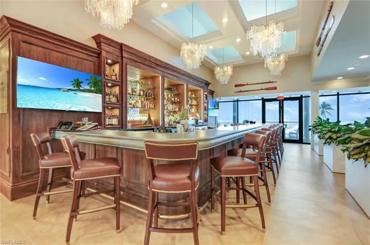 Community bar area with coffered ceiling, pendant lighting, a high ceiling, open shelves, and a chandelier