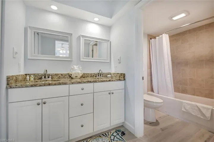 Bathroom featuring double vanity, shower / bath combination with curtain, and light wood-style flooring