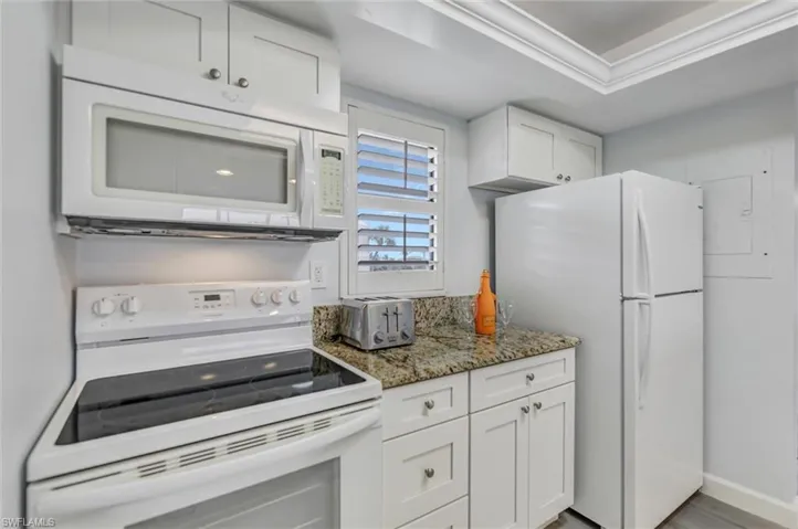 Kitchen featuring white appliances, white cabinets, light stone countertops, ornamental molding, and light wood finished floors