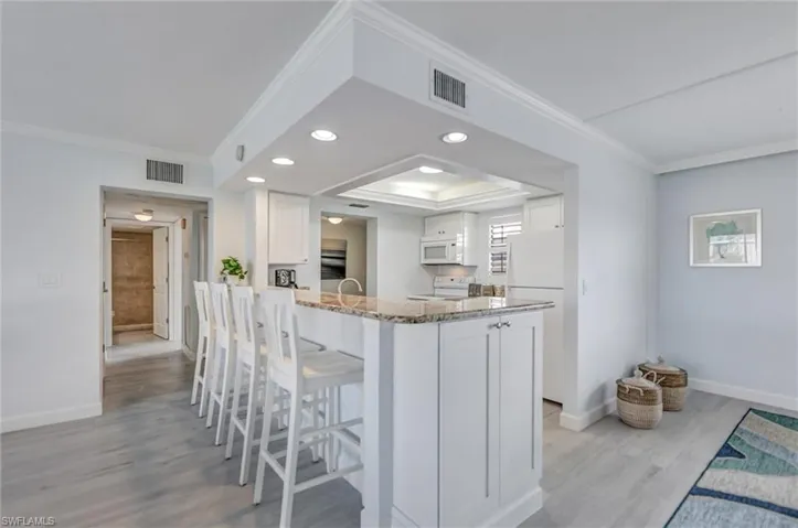 Kitchen featuring a breakfast bar area, white cabinets, recessed lighting, a peninsula, and light stone countertops