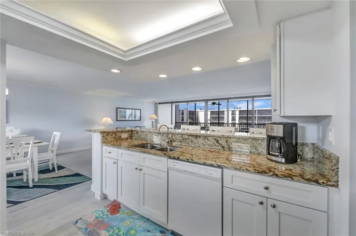 Kitchen with a peninsula, white dishwasher, white cabinetry, ornamental molding, and light stone counters
