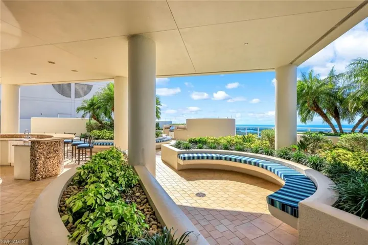 Covered section of the rooftop terrace featuring built-in seating, greenery, and open views of the coastline.