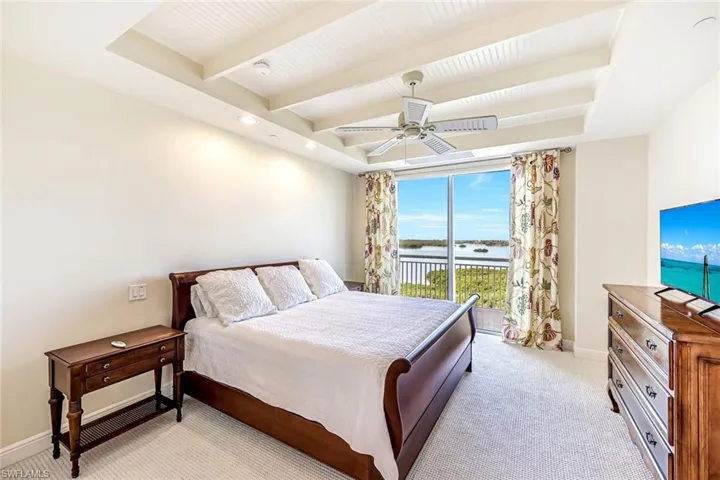 Bright guest bedroom with ceiling detail, soft flooring, and large windows framing water views.