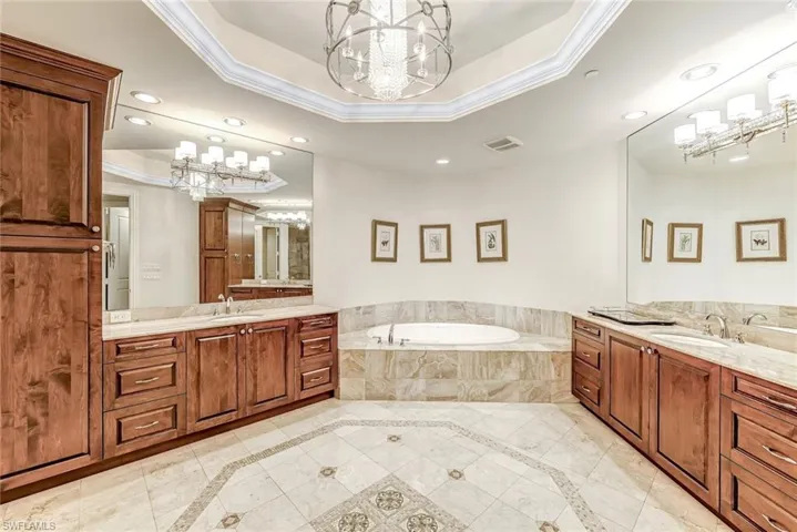 Spacious ensuite bathroom with dual vanities, wood cabinetry, large mirrors, and a soaking tub.