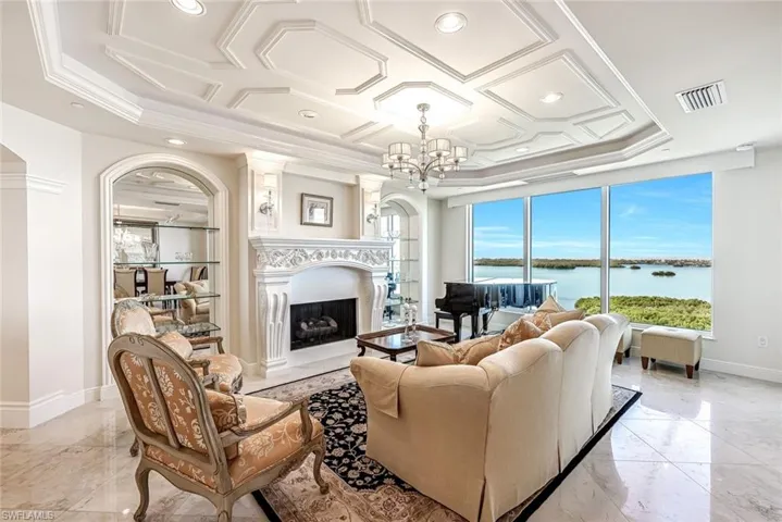 This refined living area offers a fireplace, built-in shelving, coffered ceilings, and expansive windows overlooking the water.