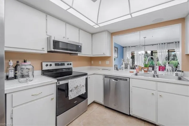 Kitchen featuring stainless steel appliances, light countertops, white cabinetry, light tile patterned floors, and pendant lighting