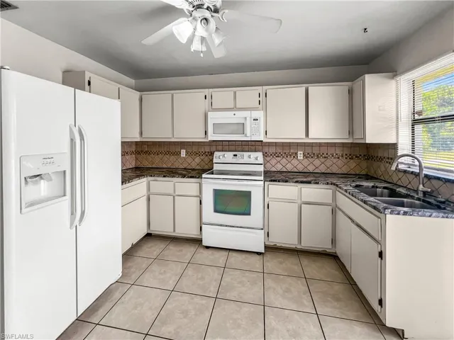Kitchen featuring white cabinetry, tile backsplash, dark countertops, a stainless steel sink, and tile flooring