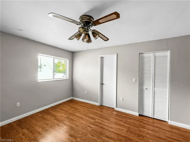 Wood-finish flooring, neutral wall tones, window with natural illumination, built-in ceiling fan, and louvered closet doors