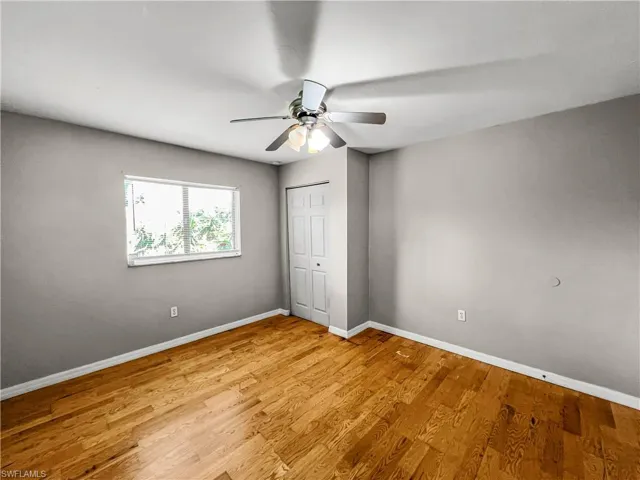 Room featuring wood-finish flooring, a ceiling fan with integrated lighting, a window, and a paneled closet door