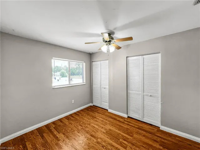 Wood-finish flooring, neutral wall paint, ceiling fan with integrated lighting, and two sets of louvered closet doors