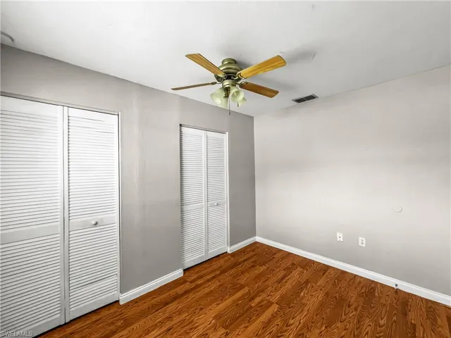 Wood-finish flooring with white baseboards, louvered bi-fold doors, and a ceiling fan with integrated lighting