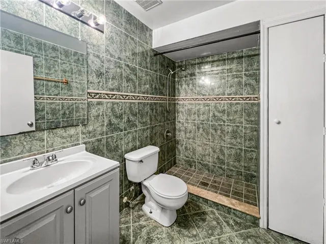 Tiled shower with decorative accent border, white vanity with integrated sink, and track lighting fixture