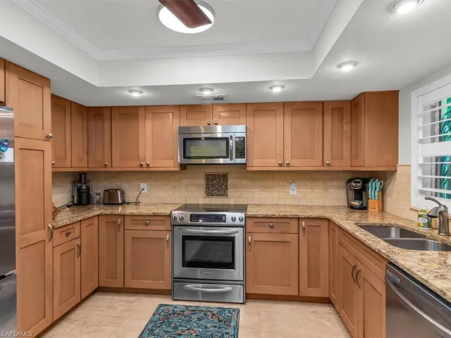 Kitchen featuring appliances with stainless steel finishes, sink, light tile  floors, decorative backsplash, and ornamental molding
