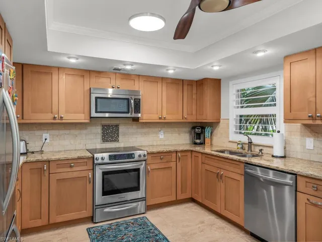 Kitchen featuring appliances with stainless steel finishes, light tile flooring, decorative backsplash, and sink