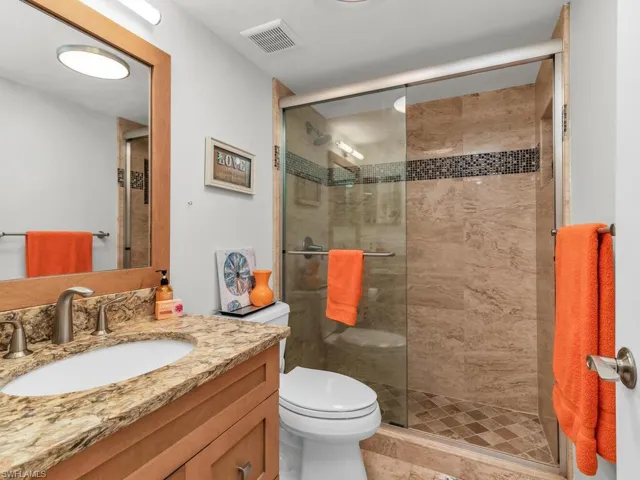 Bathroom featuring vanity, a shower with door, tile flooring, and toilet