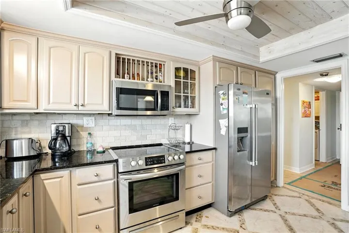 Kitchen with appliances with stainless steel finishes, inlaid floor details, backsplash, dark stone countertops, and a ceiling fan - Virtually Edited Image