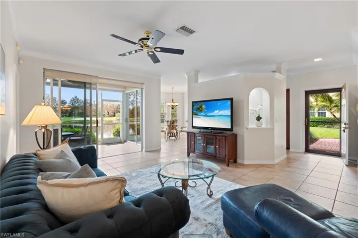 Living room featuring ceiling fan with notable chandelier, light tile patterned floors, and ornamental molding