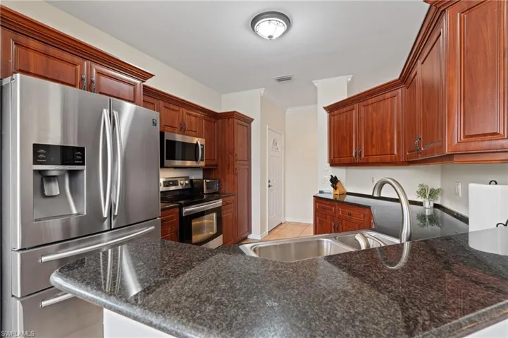 Kitchen with dark stone countertops, kitchen peninsula, sink, a breakfast bar area, and stainless steel appliances