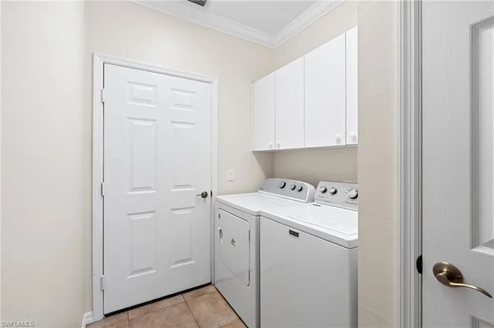 Laundry room featuring light tile patterned floors, separate washer and dryer, ornamental molding, and cabinets