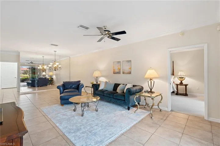 Living room featuring ceiling fan with notable chandelier, ornamental molding, and light tile patterned flooring