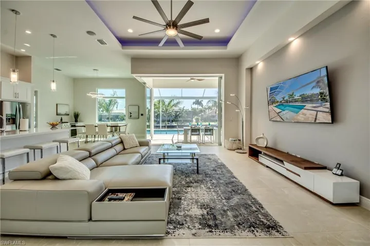 Living room with a raised ceiling, a sunroom, light tile patterned floors, recessed lighting, and a ceiling fan