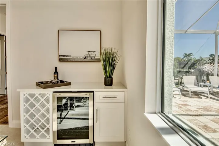 Indoor dry bar featuring white cabinetry, wine cooler, and light stone counters