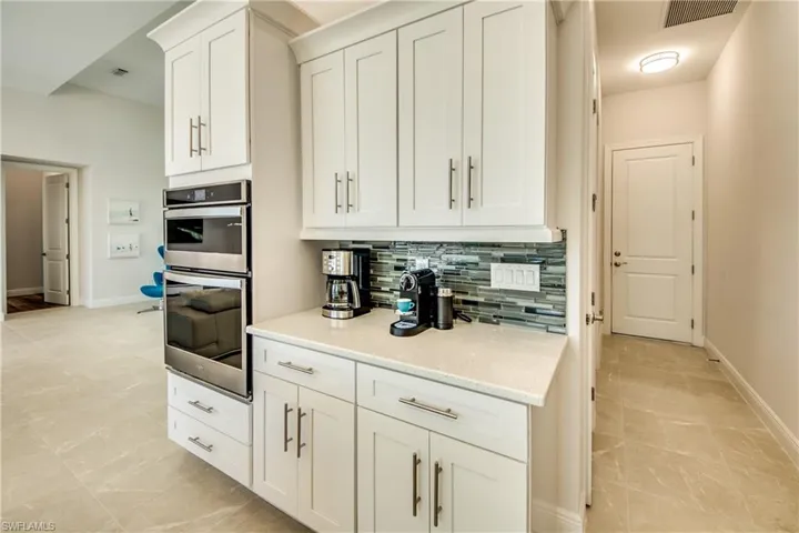 Kitchen with stainless steel double oven, white cabinetry, decorative backsplash, and light stone countertops
