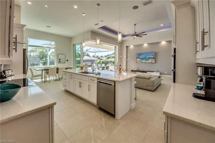 Kitchen with light stone countertops, open floor plan, white cabinets, pendant lighting, and stainless steel dishwasher