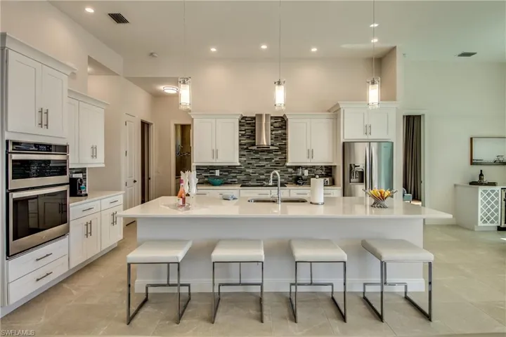 Kitchen featuring a kitchen bar, white cabinetry, appliances with stainless steel finishes, hanging light fixtures, and a kitchen island with sink