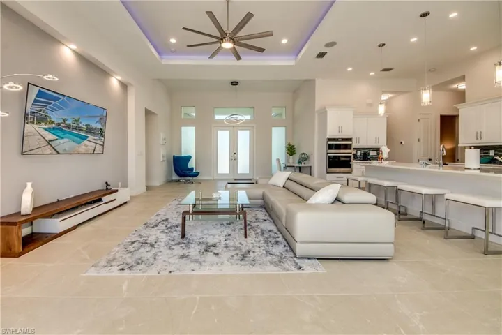 Living room with a towering ceiling, a ceiling fan, french doors, recessed lighting, and a tray ceiling