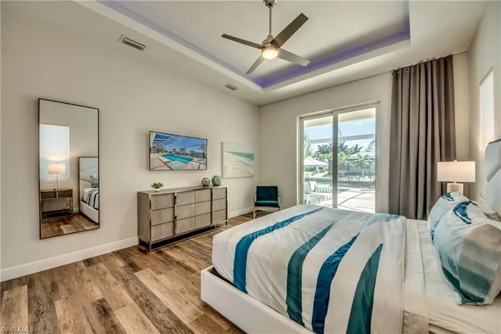 Bedroom featuring a raised ceiling, access to outside, wood finished floors, and a ceiling fan